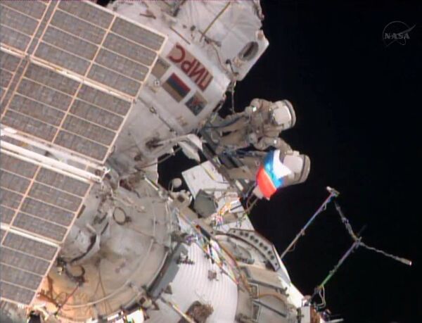 A cosmonaut unfurls a Russian flag outside the ISS during a spacewalk on Thursday to mark Russian Flag Day. - Sputnik International